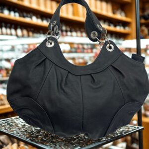 Image 1: Black leather pleated hobo bag with silver ring hardware displayed on a stand.