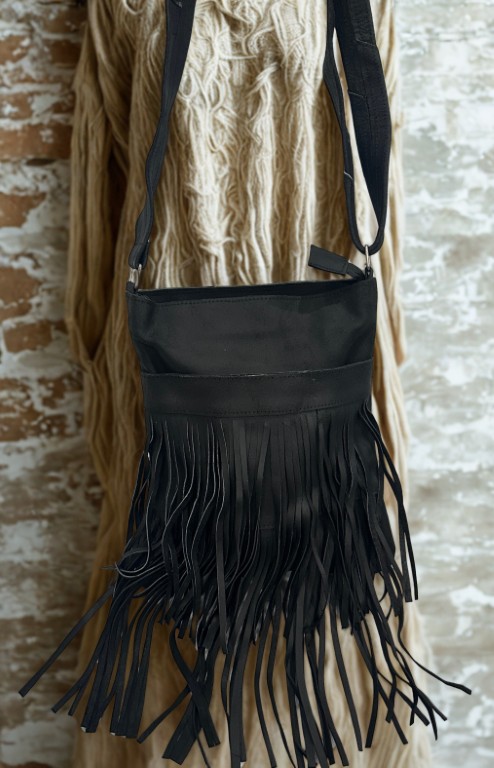 Image 1: Black leather fringe crossbody bag hanging on a display.